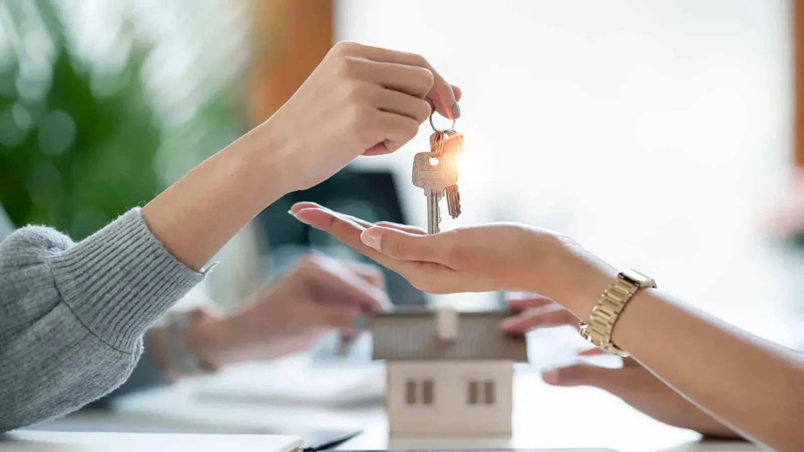 House keys being handed over across a table with a model home